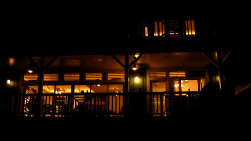 exterior night time shot of the living room (lower left) and kitchen (lower right) . Note the continuous row of louvers above the windows and sliding glass doors. This allows the entire house to 'breath', a hallmark of DAK designed homes.